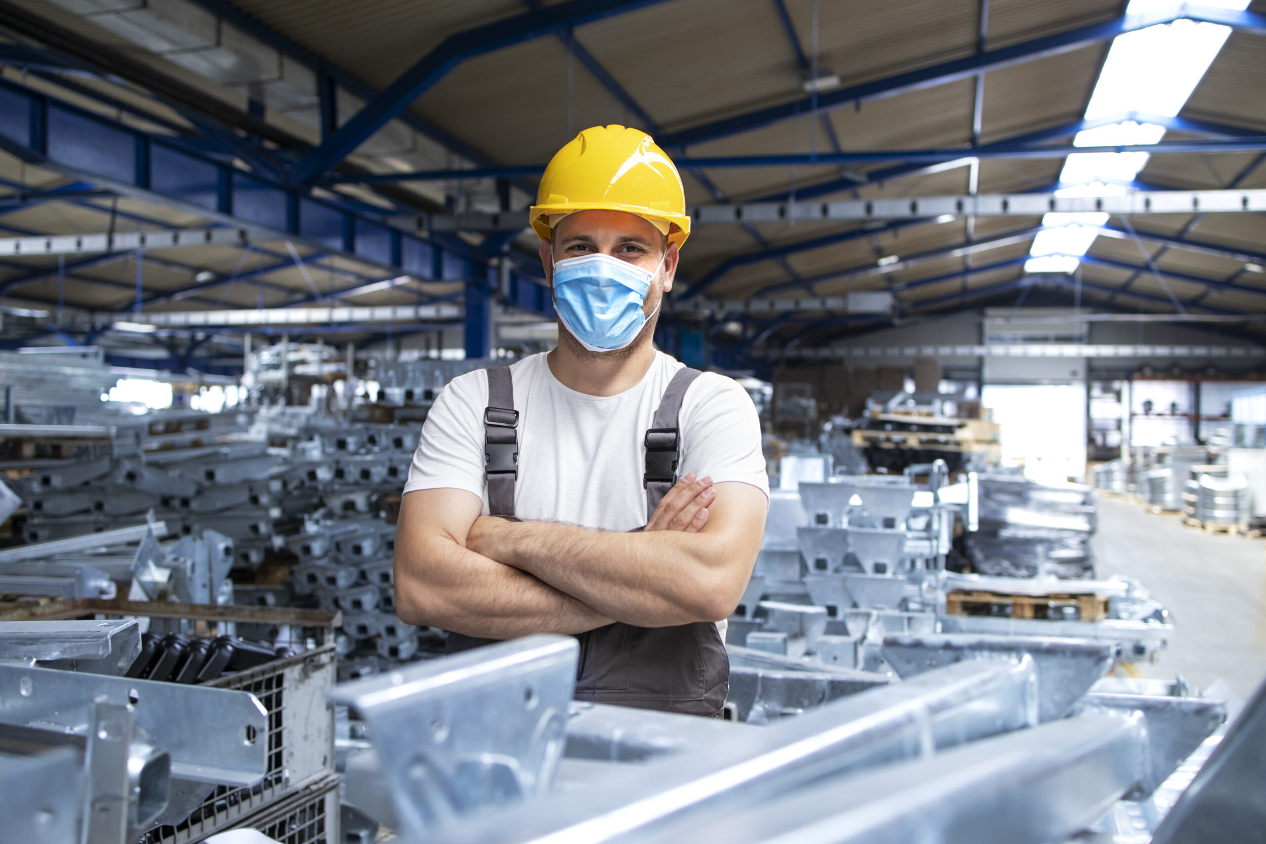 Portrait of factory workman in uniform and hardhat wearing face mask in industrial production plant.